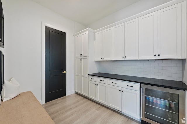 4784 W Juniper Bend Cir, Herriman, UT 84096 - kitchen featuring light wood finished floors, tasteful backsplash, dark countertops, beverage cooler, and white cabinetry