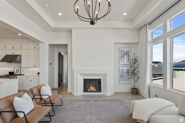 4784 W Juniper Bend Cir, Herriman, UT 84096 - living area with a chandelier, a tray ceiling, light wood-style flooring, recessed lighting, and a glass covered fireplace