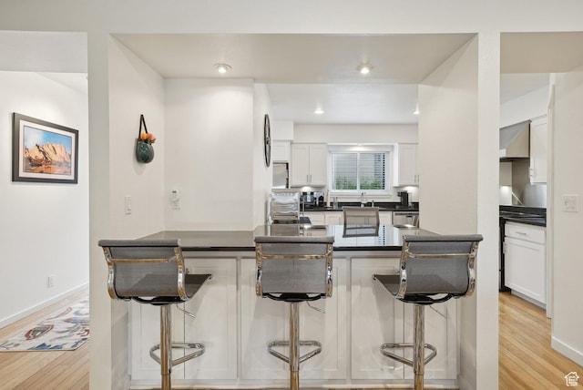71 W Apricot Ave, Salt Lake City, UT 84103 - kitchen featuring light wood-type flooring, dark countertops, a breakfast bar area, and white cabinets