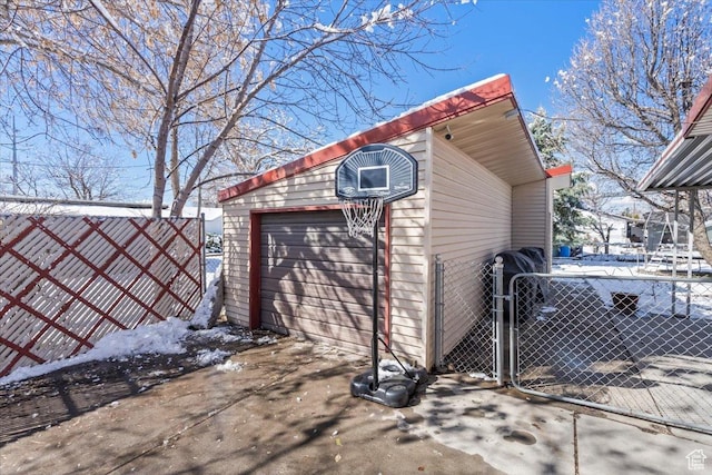 snow covered structure with an outdoor structure, a gate, and fence