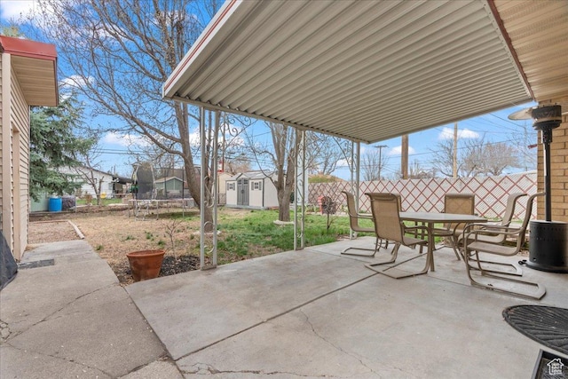 view of patio with fence, a trampoline, a storage unit, outdoor dining space, and an outbuilding