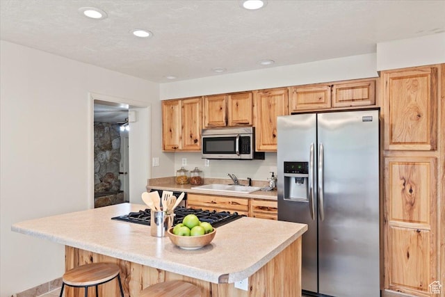kitchen featuring a kitchen bar, a sink, stainless steel appliances, light countertops, and a kitchen island