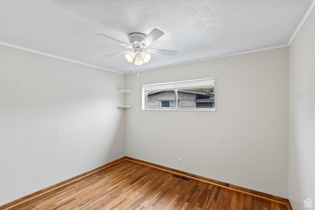 spare room with wood finished floors, visible vents, crown molding, a ceiling fan, and baseboards