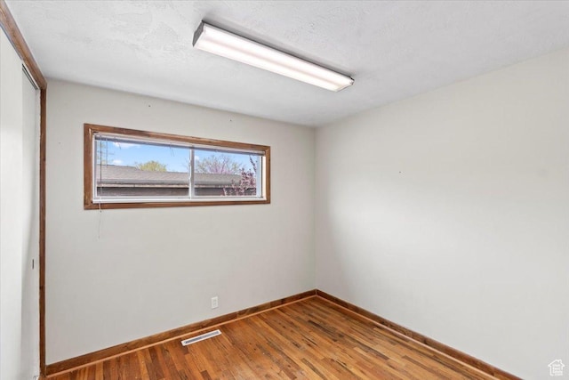 unfurnished room featuring baseboards, visible vents, and wood finished floors