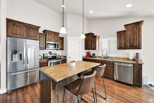 kitchen featuring light stone counters, dark wood-style flooring, dark brown cabinetry, appliances with stainless steel finishes, and a center island