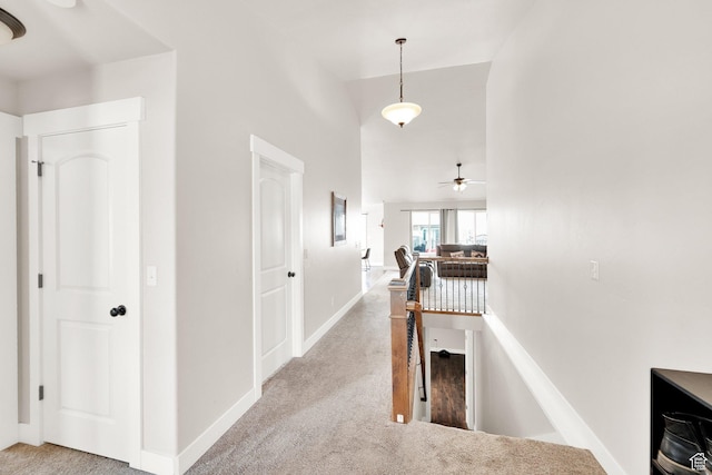 hall featuring baseboards, a towering ceiling, and light carpet