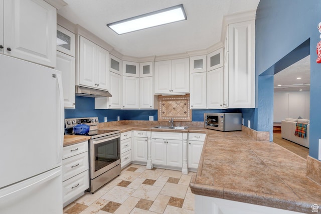 kitchen with under cabinet range hood, a sink, stainless steel appliances, white cabinets, and glass insert cabinets