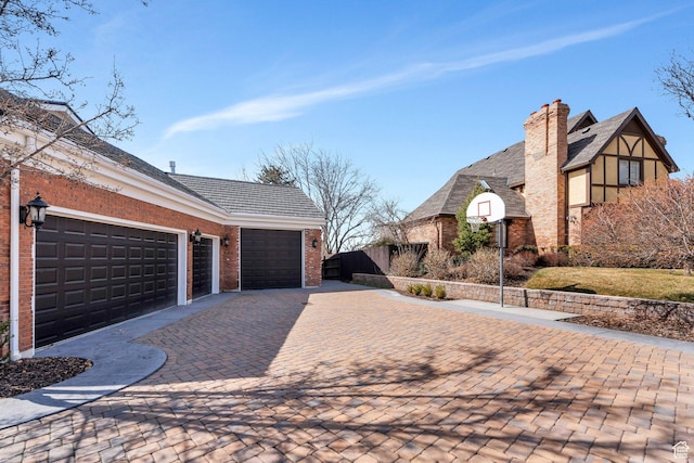 view of home's exterior with brick siding, fence, a chimney, decorative driveway, and a garage