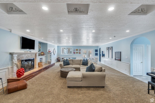 living room with carpet, arched walkways, ornamental molding, wainscoting, and a tiled fireplace