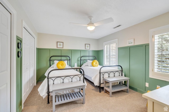 bedroom with light carpet, a decorative wall, visible vents, and a wainscoted wall