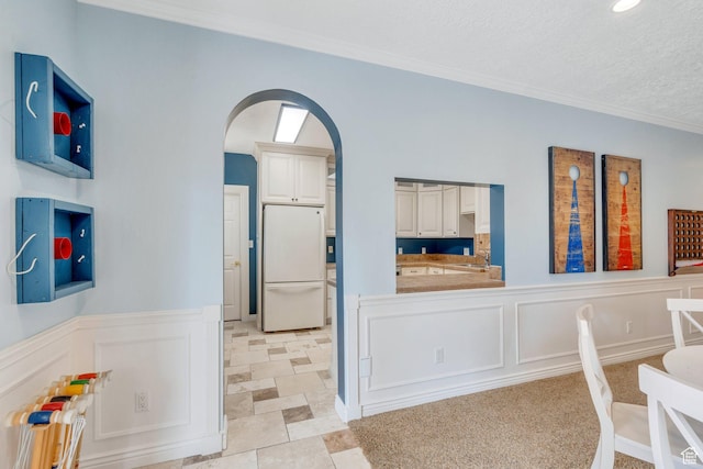 interior space with arched walkways, crown molding, wainscoting, and a decorative wall