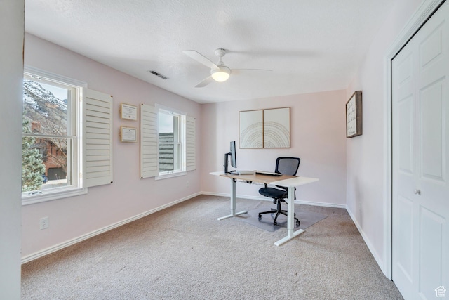 carpeted office space with a textured ceiling, baseboards, visible vents, and ceiling fan