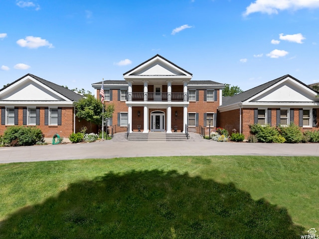 neoclassical / greek revival house with a front lawn, a balcony, french doors, and brick siding