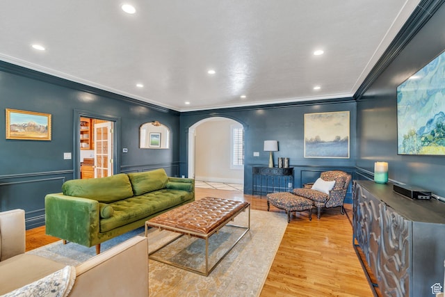 living area with crown molding, a wainscoted wall, recessed lighting, light wood-style floors, and arched walkways