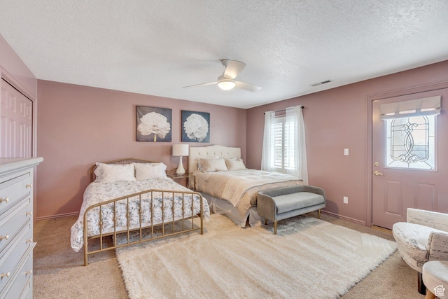 bedroom featuring visible vents, a textured ceiling, baseboards, light colored carpet, and ceiling fan