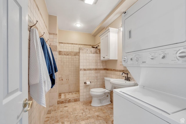 bathroom featuring a tile shower, tile walls, stacked washer / drying machine, and a sink