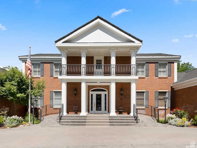 greek revival house featuring a porch, a balcony, and brick siding