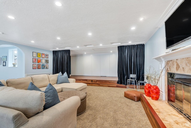 living area featuring carpet, a tiled fireplace, recessed lighting, arched walkways, and a textured ceiling