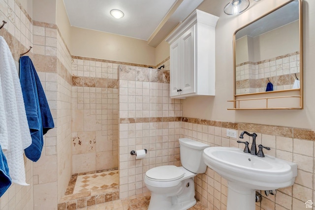 bathroom featuring a sink, tiled shower, toilet, and tile walls