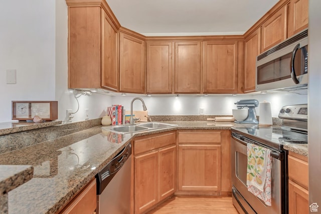 kitchen featuring a sink, light wood-style flooring, light stone counters, and stainless steel appliances