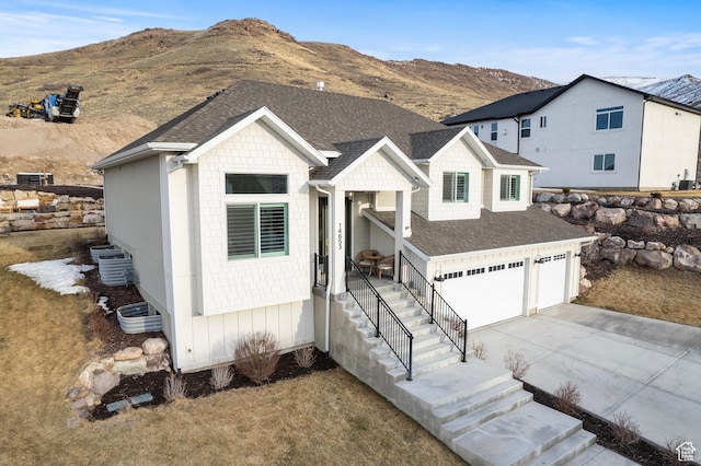 modern farmhouse featuring an attached garage, a mountain view, driveway, and roof with shingles
