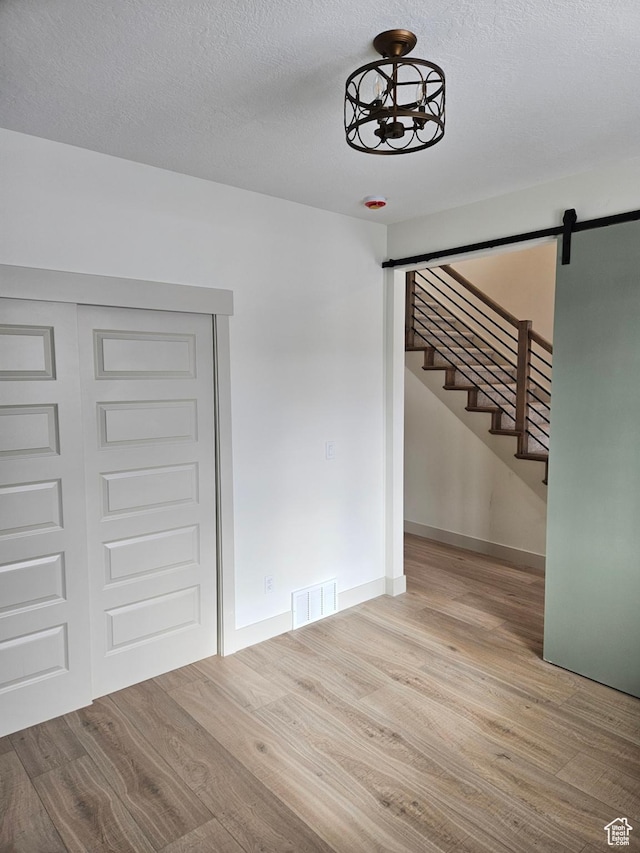 unfurnished dining area featuring wood finished floors, a barn door, stairway, baseboards, and a textured ceiling