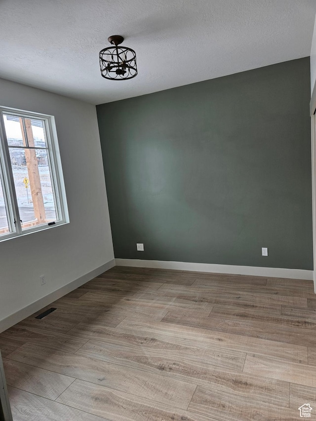 unfurnished room featuring wood finished floors, a textured ceiling, and baseboards