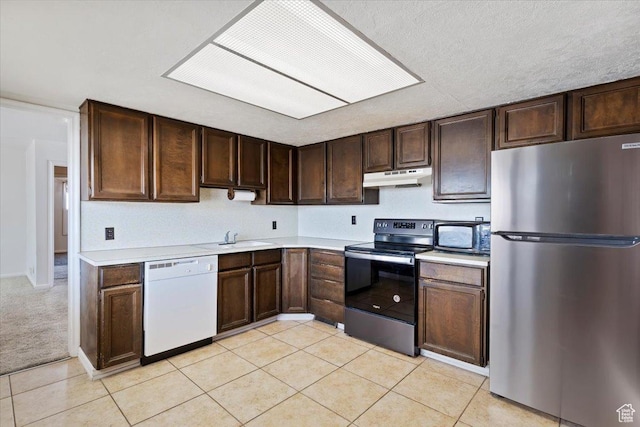 kitchen with dark brown cabinets, light countertops, under cabinet range hood, stainless steel appliances, and light tile patterned flooring