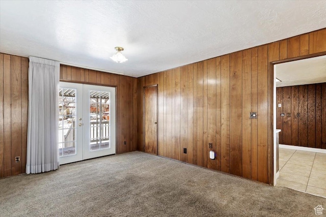 carpeted empty room with french doors, a textured ceiling, and wooden walls