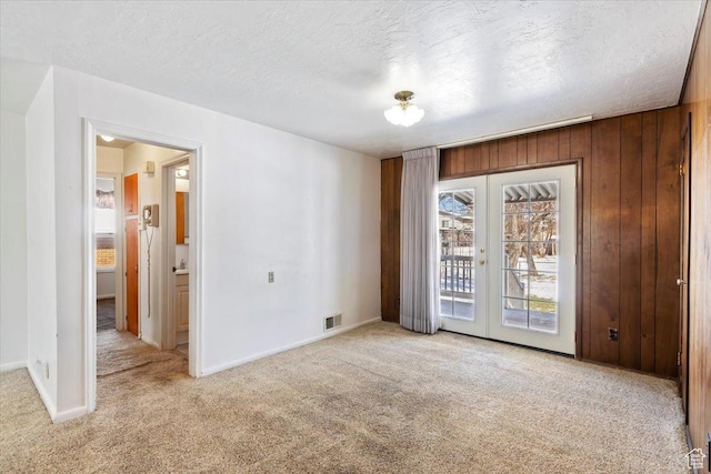 carpeted spare room featuring visible vents, baseboards, wooden walls, a textured ceiling, and french doors