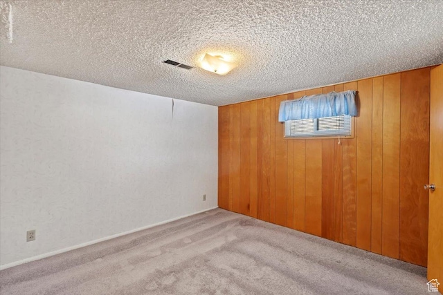 empty room featuring wooden walls, carpet flooring, a textured ceiling, and visible vents