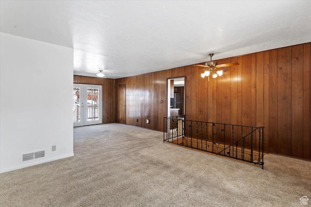 unfurnished living room with carpet floors, visible vents, wooden walls, french doors, and a ceiling fan
