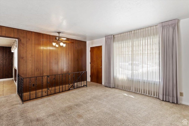 carpeted spare room with ceiling fan and wood walls
