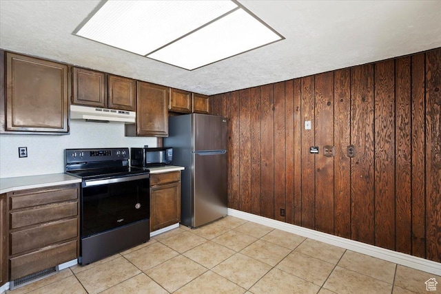 kitchen featuring freestanding refrigerator, black microwave, wooden walls, electric range oven, and under cabinet range hood
