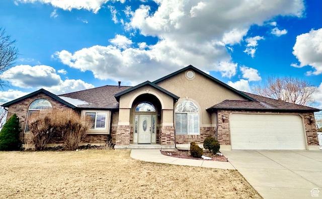 view of front of property with stucco siding, driveway, an attached garage, a shingled roof, and brick siding