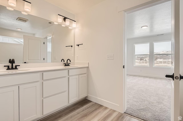 bathroom with a textured ceiling, double vanity, a sink, and visible vents