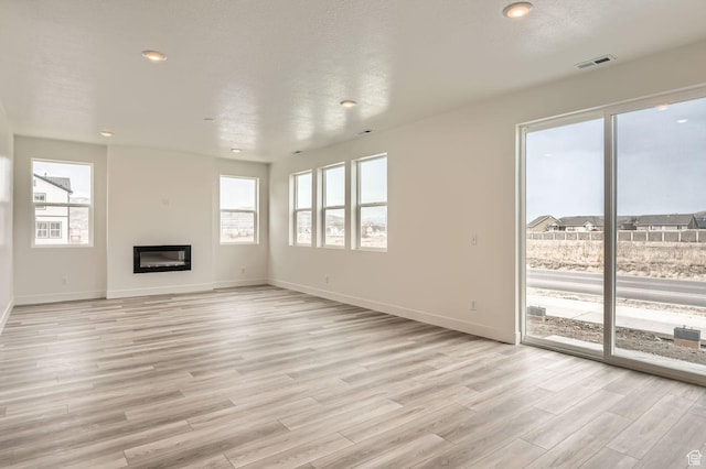 unfurnished living room featuring a glass covered fireplace, baseboards, recessed lighting, light wood-style flooring, and a textured ceiling