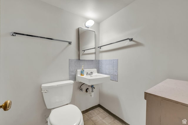 bathroom with toilet, a sink, tasteful backsplash, tile patterned flooring, and baseboards