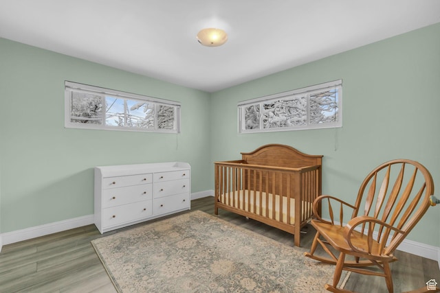 bedroom with a nursery area, baseboards, and wood finished floors