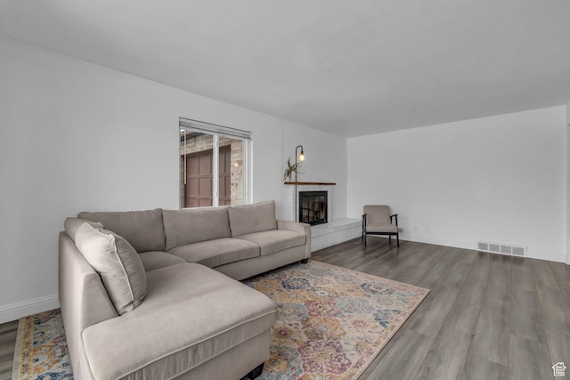 living area with visible vents, baseboards, a fireplace with raised hearth, and wood finished floors