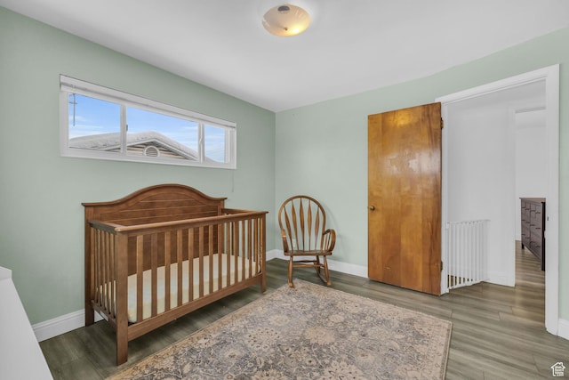 bedroom featuring baseboards, a nursery area, wood finished floors, and radiator heating unit