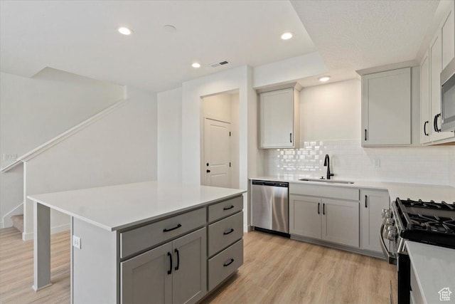 kitchen featuring appliances with stainless steel finishes, a sink, gray cabinetry, light wood-style floors, and light countertops