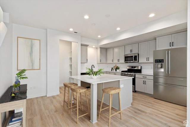 kitchen featuring stainless steel appliances, a kitchen breakfast bar, decorative backsplash, a kitchen island, and gray cabinetry