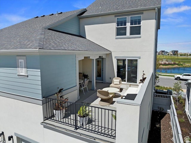 back of house featuring roof with shingles, stucco siding, a water view, and a patio