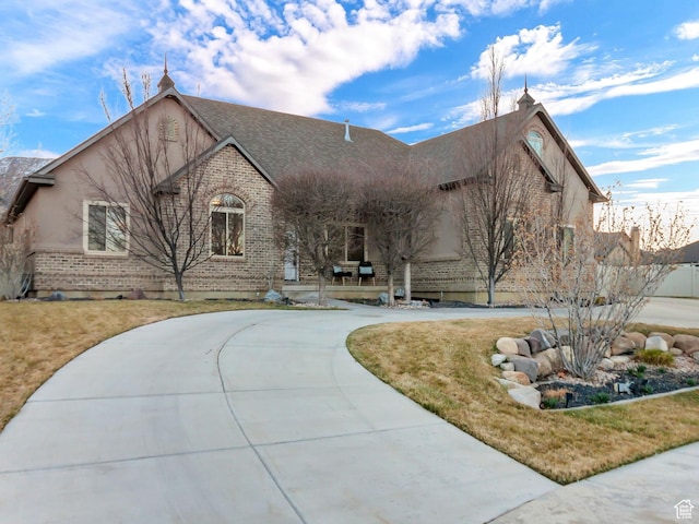 view of front of property with brick siding, a front lawn, a porch, stucco siding, and driveway