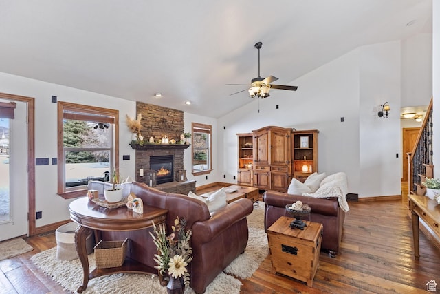 living room with baseboards, stairs, hardwood / wood-style floors, a stone fireplace, and a ceiling fan