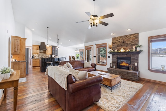 living room with baseboards, a stone fireplace, light wood-style flooring, high vaulted ceiling, and a ceiling fan