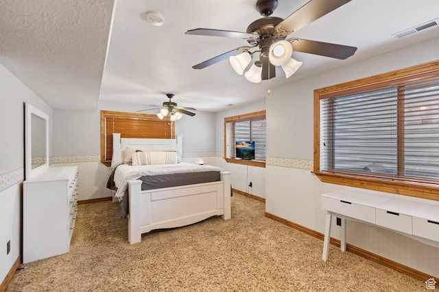 bedroom featuring visible vents, a wainscoted wall, light carpet, a textured ceiling, and a ceiling fan