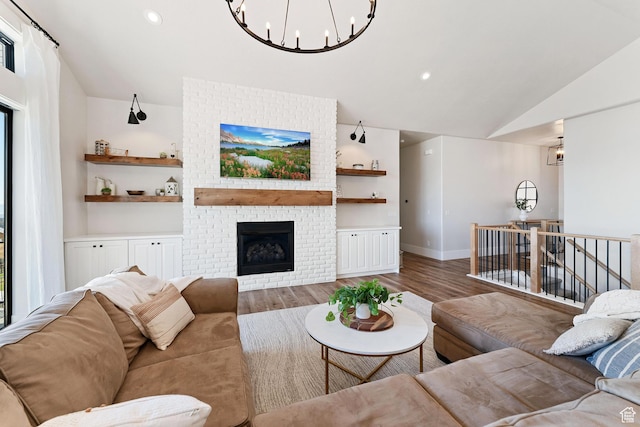 living room with lofted ceiling, wood finished floors, baseboards, a brick fireplace, and a chandelier