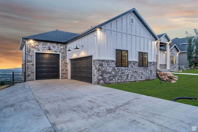 view of front of property featuring board and batten siding, a shingled roof, a yard, a garage, and driveway